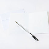 Pen laying on a blank greeting card and white envelope on a white background
