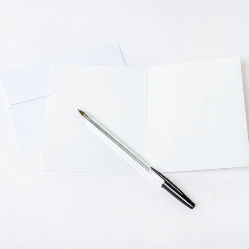 Pen laying on a blank greeting card and white envelope on a white background
