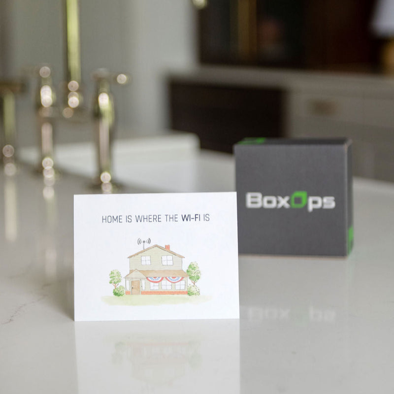 Humorous new homeowner greeting card sitting on a kitchen counter in front of a BoxOps gift box.
