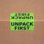 Green moving label on a brown cardboard box with text 'UNPACK FIRST'