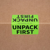 Green moving label on a brown cardboard box with text 'UNPACK FIRST'