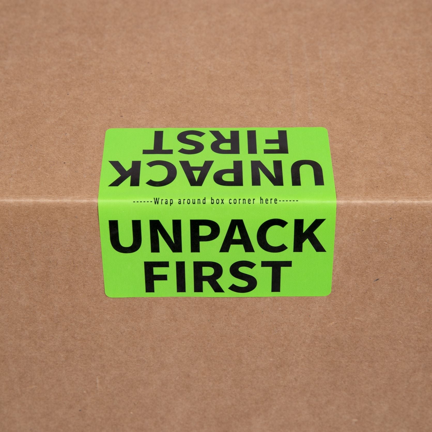 Green moving label on a brown cardboard box with text 'UNPACK FIRST'
