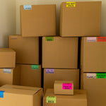 A group of cardboard moving boxes with color-coded moving labels to sort boxes by rooms and categories.