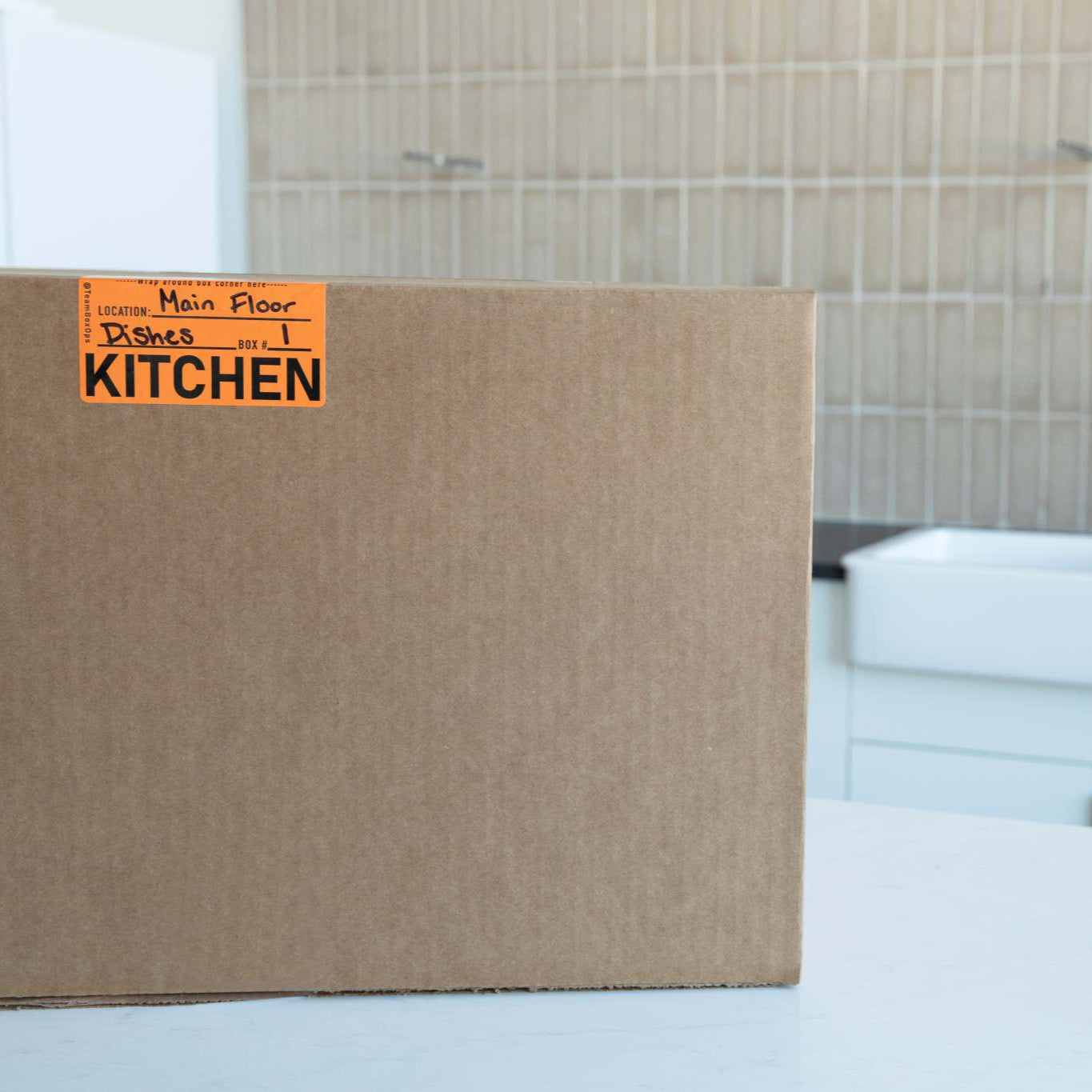 Cardboard moving box labeled 'Kitchen' in a kitchen setting.