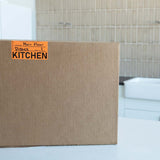 Cardboard moving box labeled 'Kitchen' in a kitchen setting.