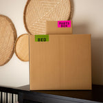 Cardboard box labeled 'Pants Box' and 'Bed' on a shelf with decorative items in the background.