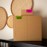 Cardboard box labeled 'Pants Box' and 'Bed' on a shelf with decorative items in the background.