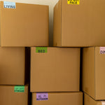 Stack of cardboard boxes with various color coded moving box stickers on a beige background