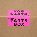 Pink 'PARTS BOX' label on a cardboard moving box for organizing parts and hardware.