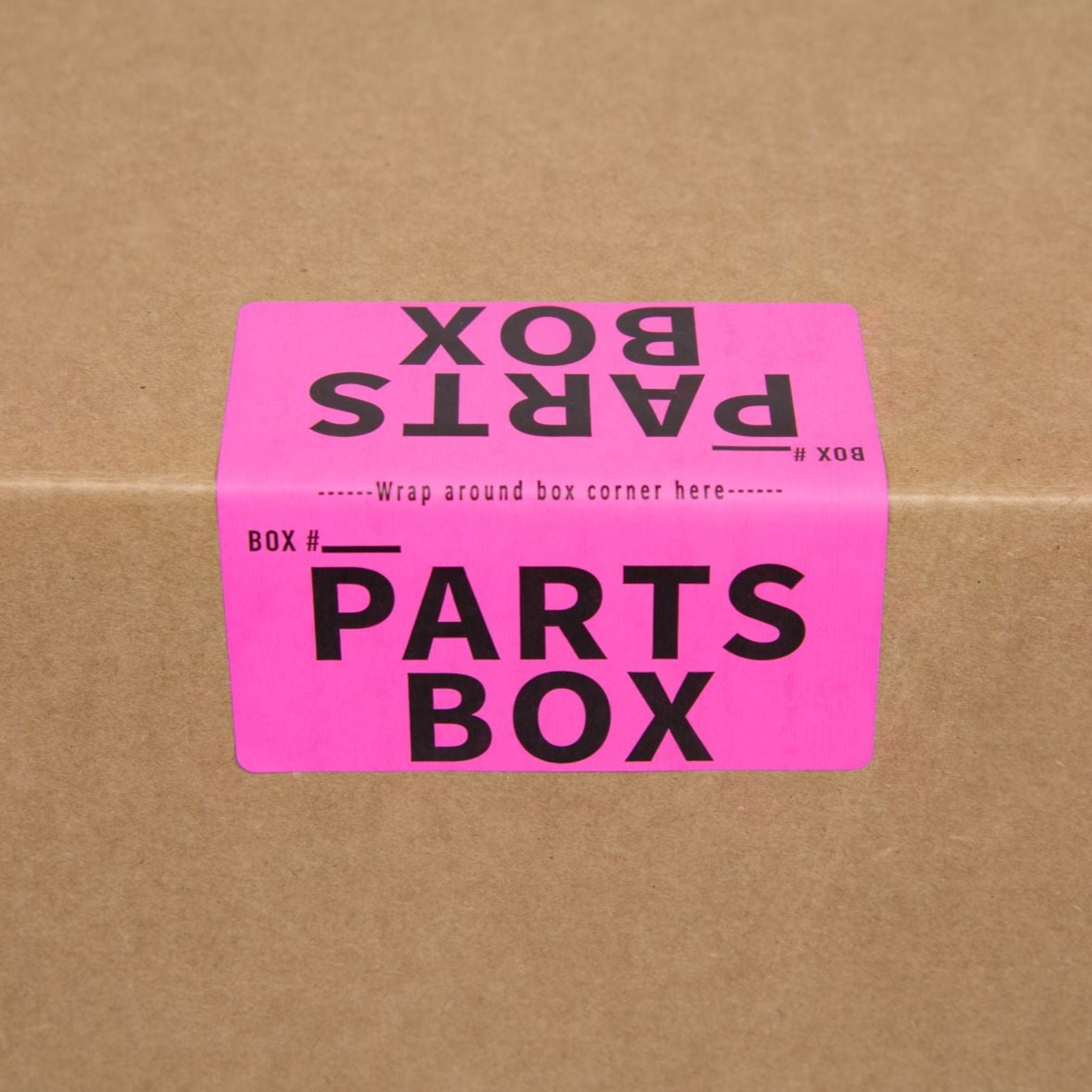 Pink 'PARTS BOX' label on a cardboard moving box for organizing parts and hardware.