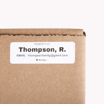 A small white sticker label with a name and contact information on it for finding missing moving boxes.