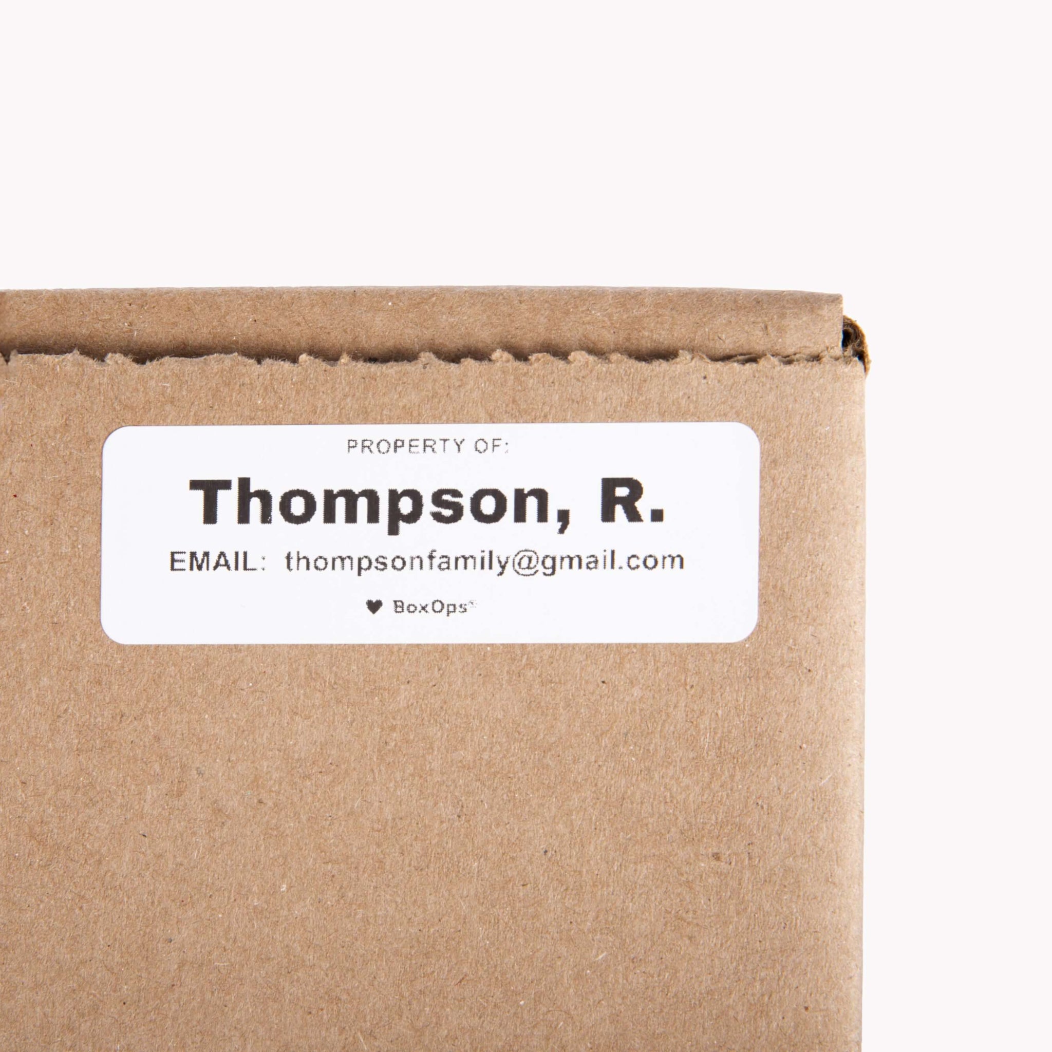 A small white sticker label with a name and contact information on it for finding missing moving boxes.