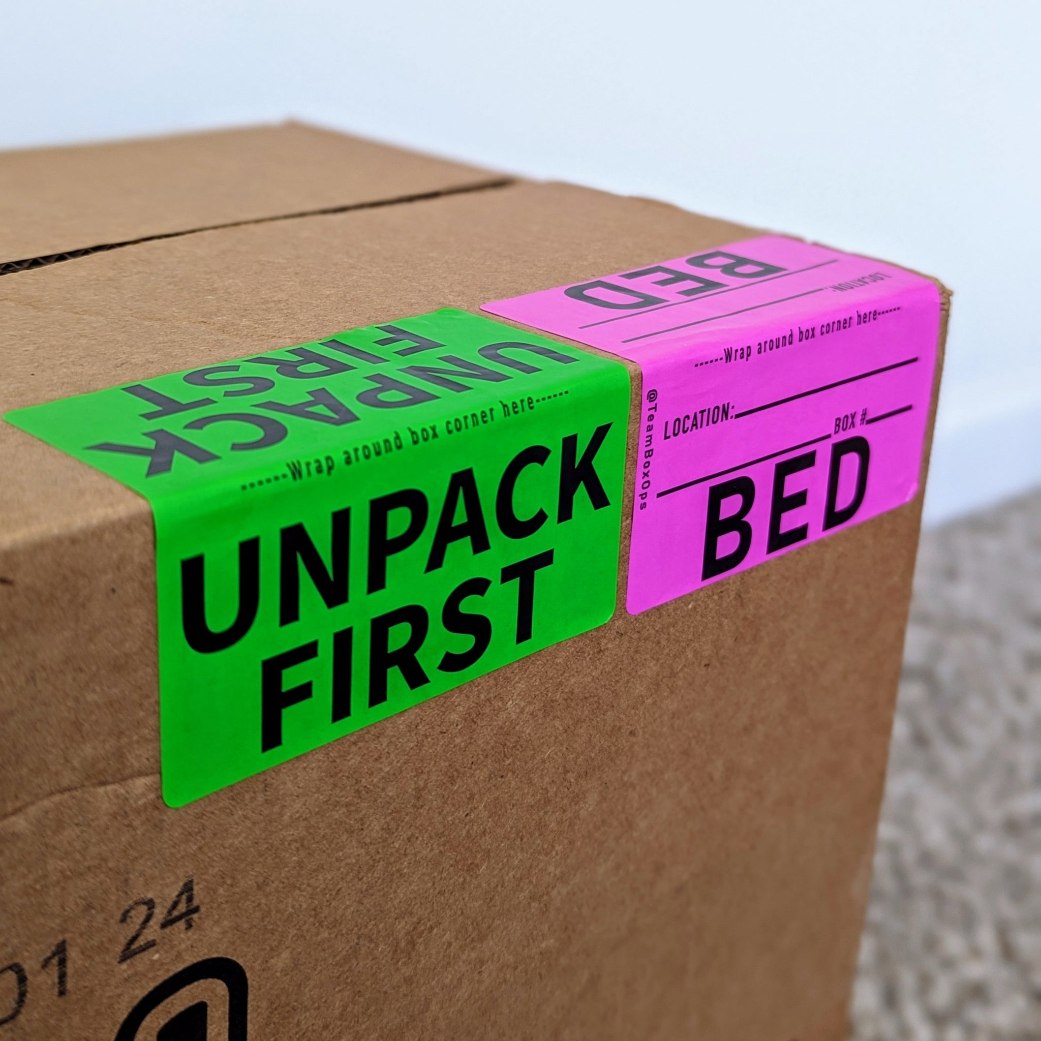 Cardboard box with 'Unpack First' and 'Bed' labels on a neutral background